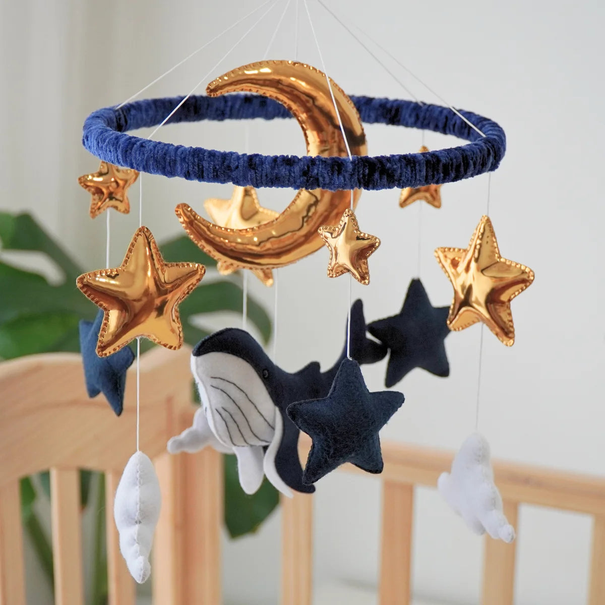 Ocean Whale felt mobile hanging above a crib with the navy whale and gold moon in view