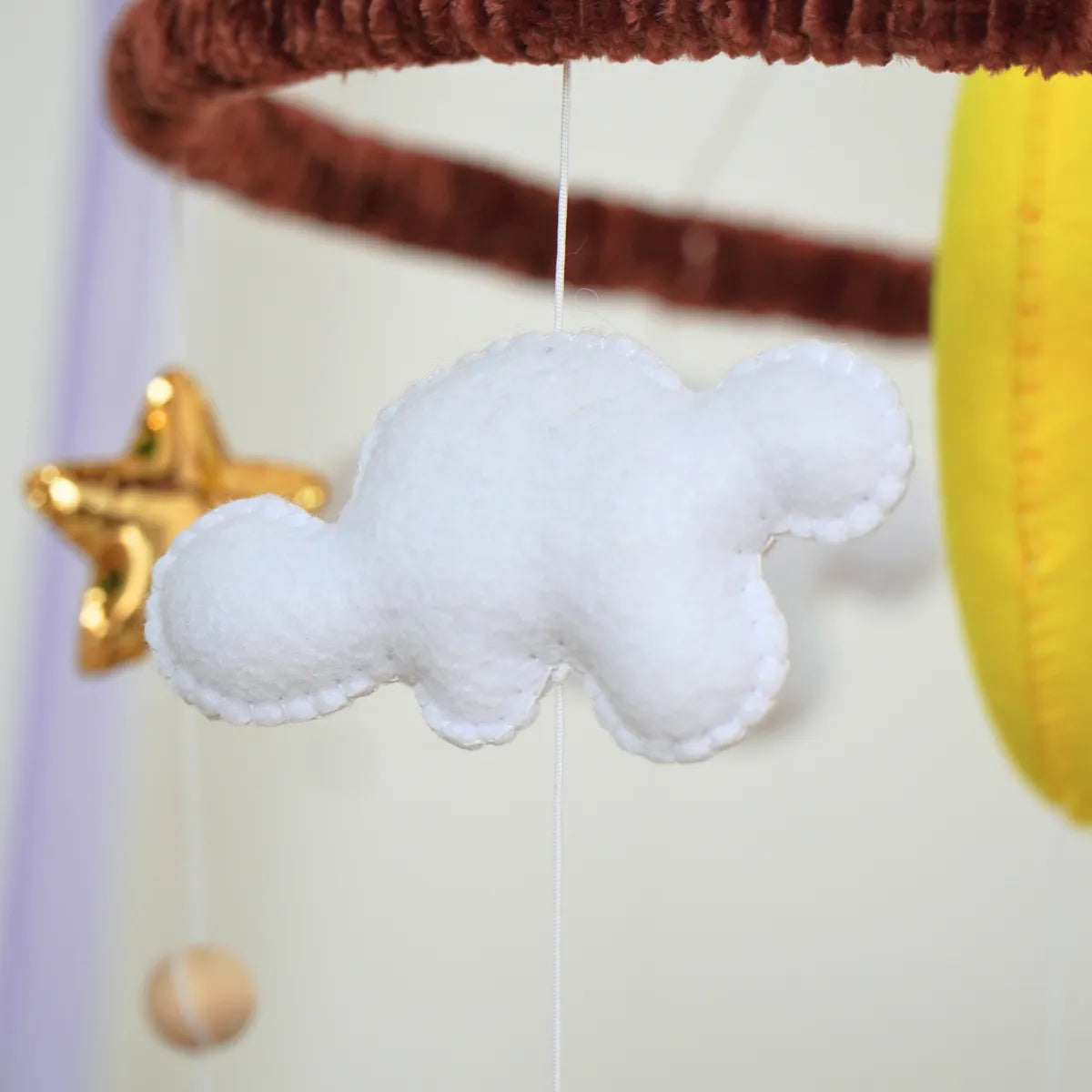 Close-up of a white felt cloud, gold star and natural wood bead on the Woodland Bear mobile